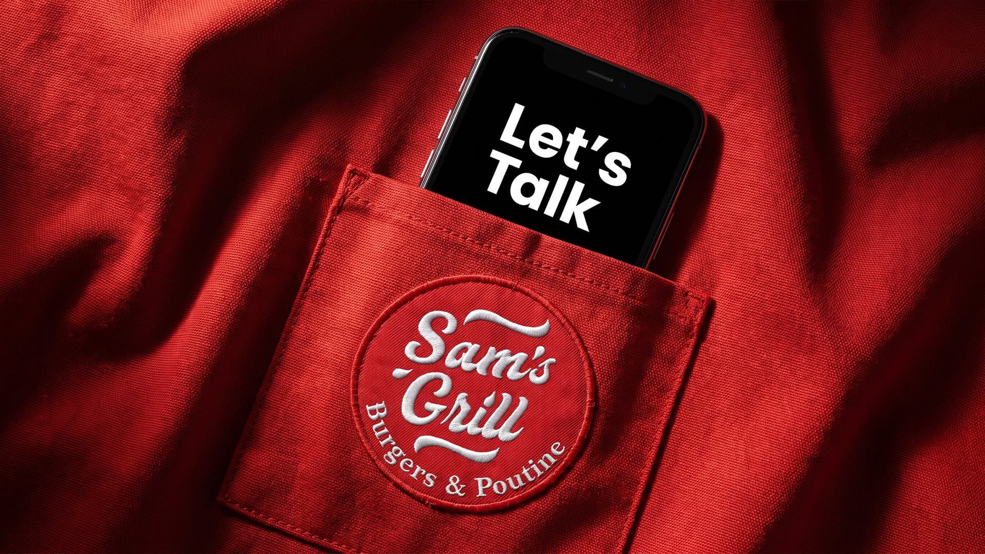 A phone reading “Let’s Talk” in the pocket of a red Sam's Grill apron